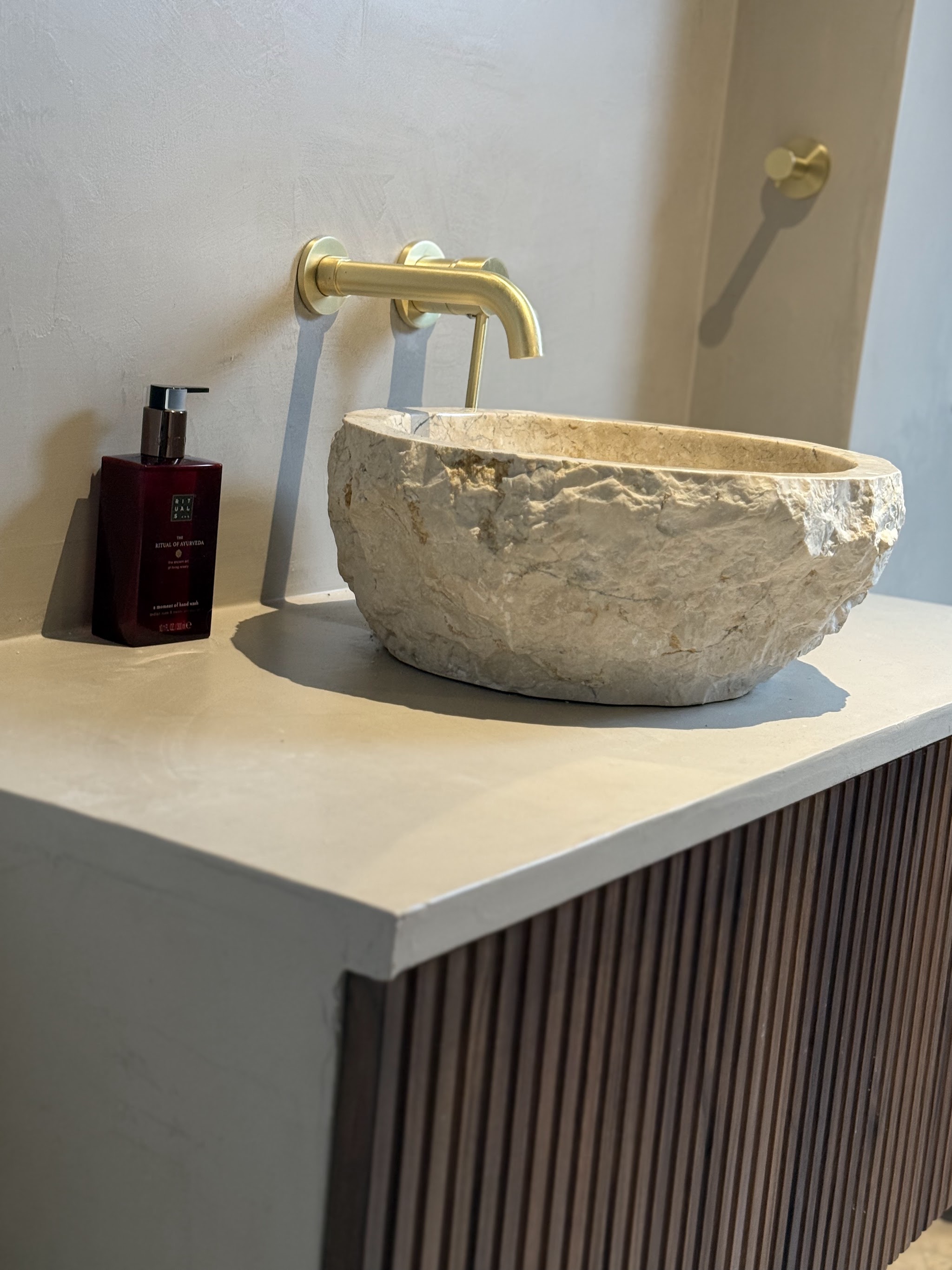 Detail van een stenen waskom met gouden kraan tegen een gestucte wand