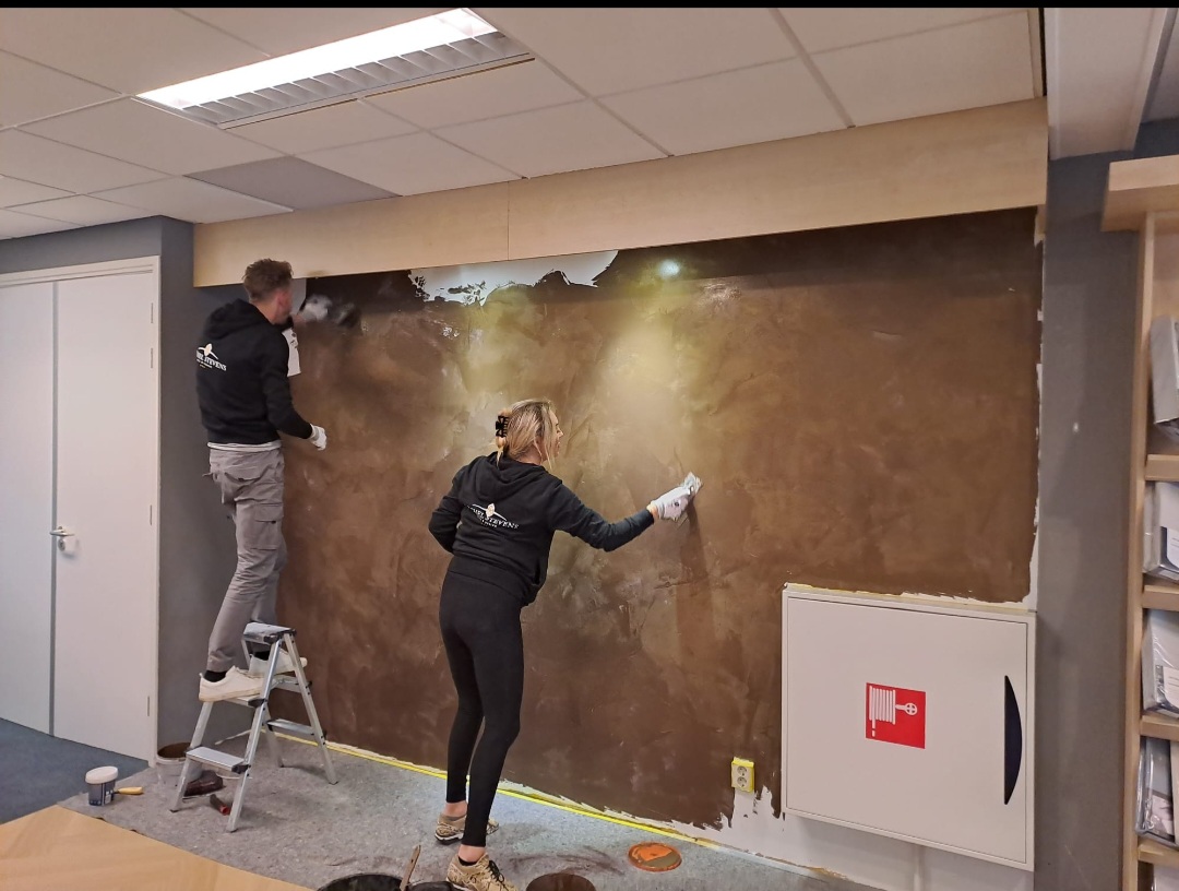 Michel en een collega brengen een bruine designwand aan in een bedrijfsruimte